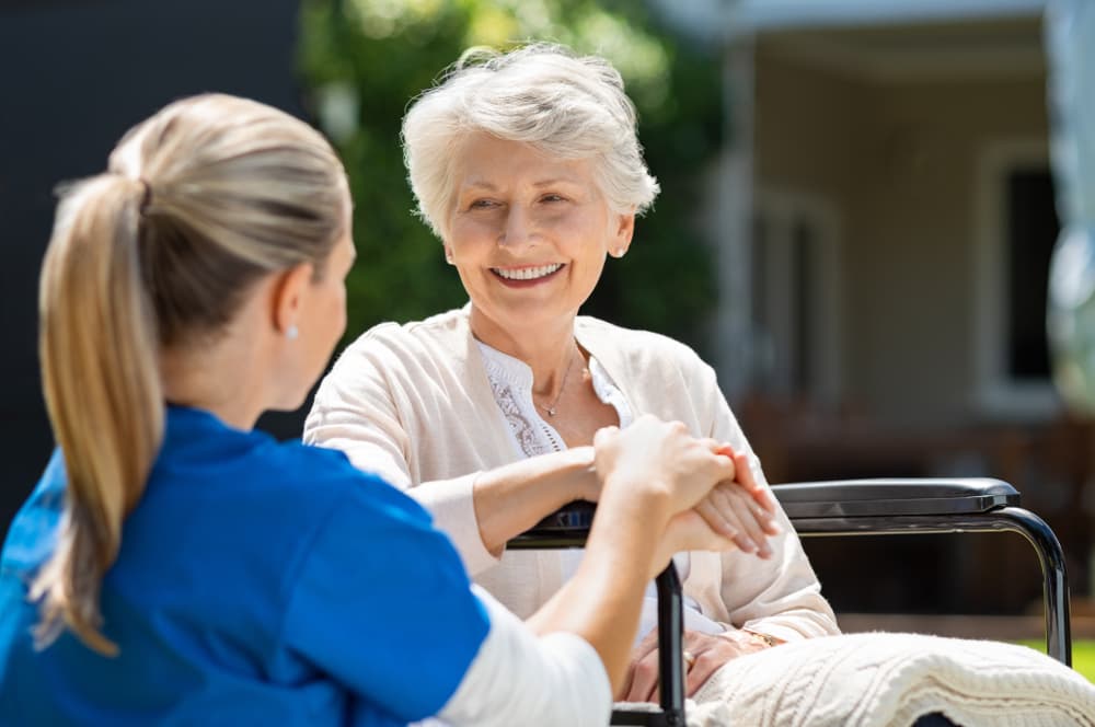 Cuidadora conversando y sonriendo con una señora mayor en el jardín